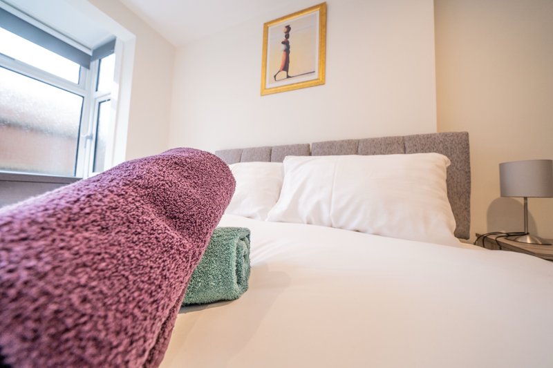 Bedroom with double bed, gray headboard, purple throw blanket, and window with natural light