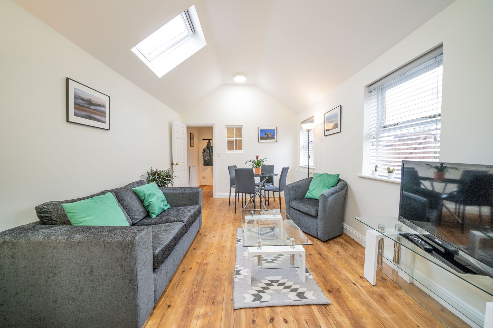 Modern living room with grey sofas, green cushions, wooden floor and skylight