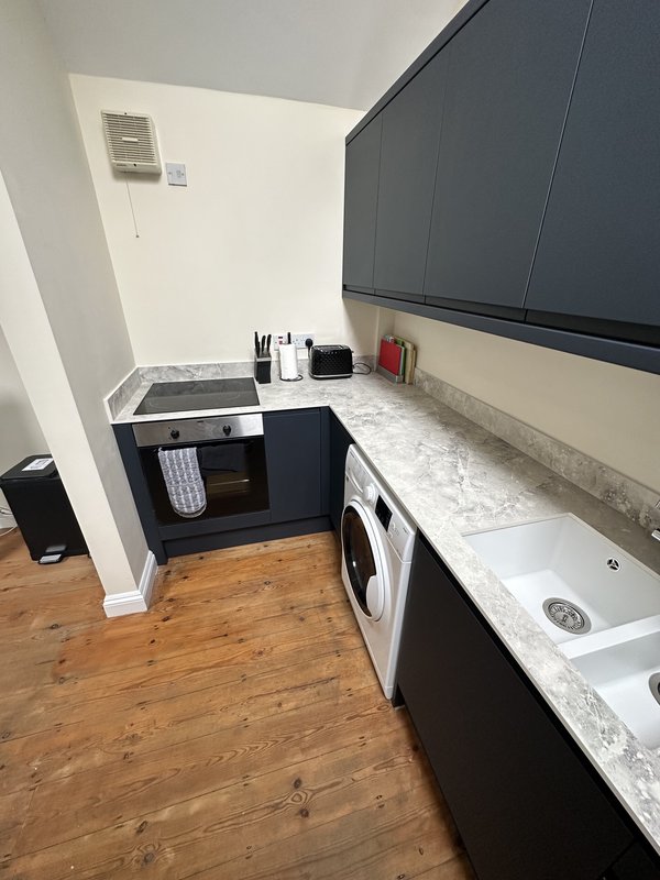 Compact kitchenette with black cabinetry, marble countertop, cooktop and washing machine