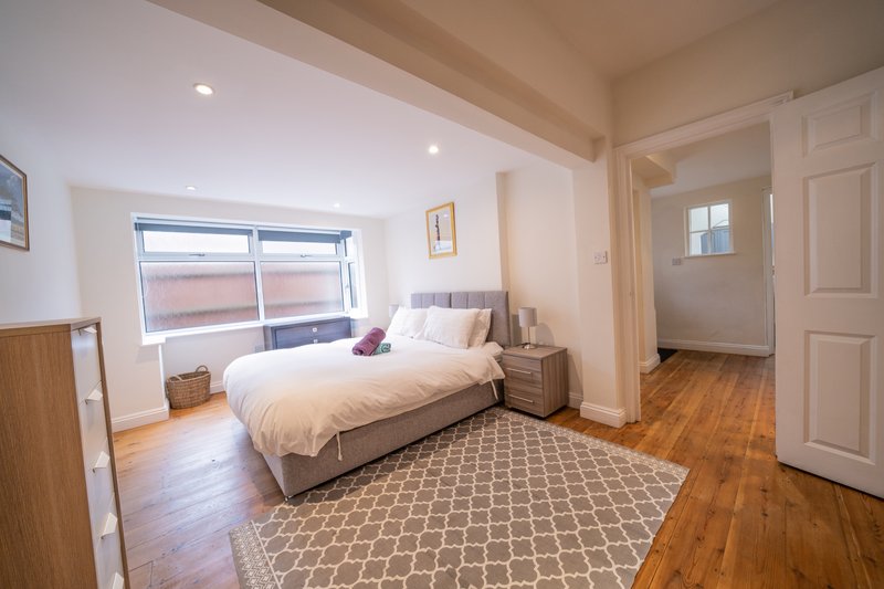 Bright bedroom with double bed, wooden floor, geometric rug and large window