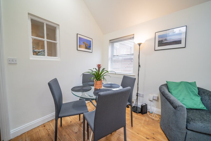 Bright dining area with round table, grey chairs, potted plant and sofa against white walls