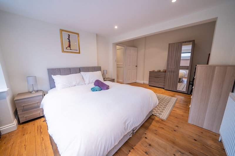 Spacious bedroom with double bed, wooden flooring, gray headboard, and ensuite bathroom access