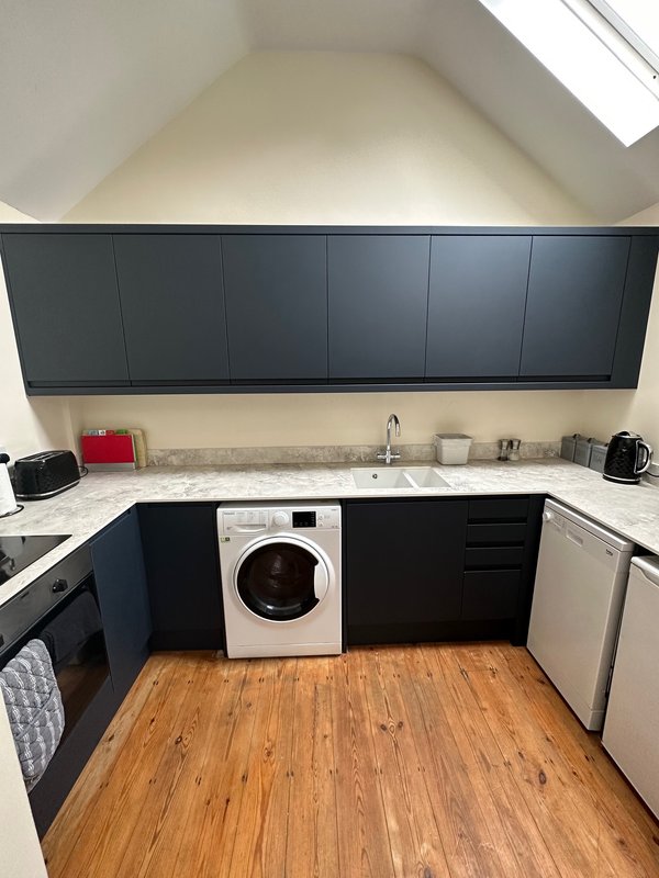 Modern kitchen with dark cabinetry, white countertop, washing machine, and wooden flooring