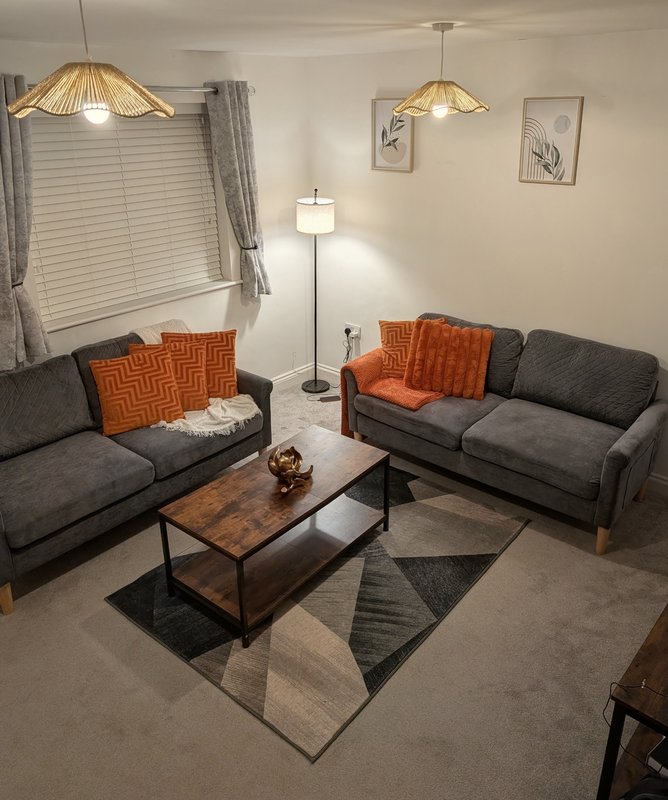 Modern living room with two gray sofas, orange cushions, wooden coffee table, and pendant lighting