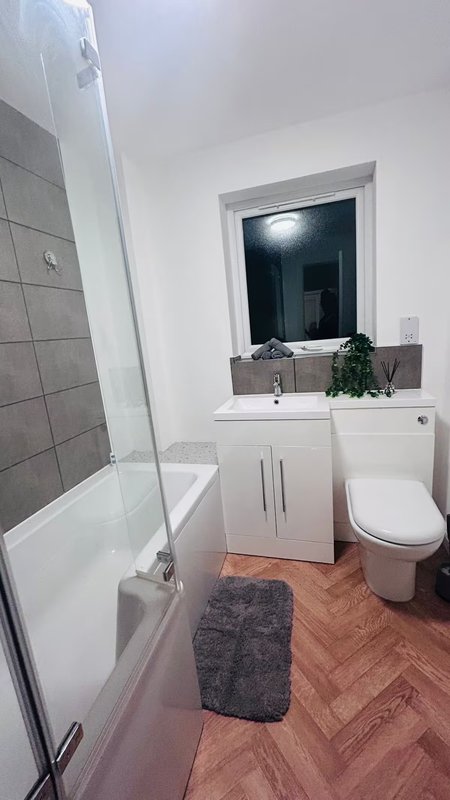 Modern bathroom with white vanity, toilet, shower enclosure, and herringbone flooring