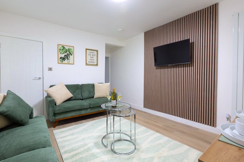 Modern living room with green sofa, wall-mounted TV, wooden slat accent wall and side table