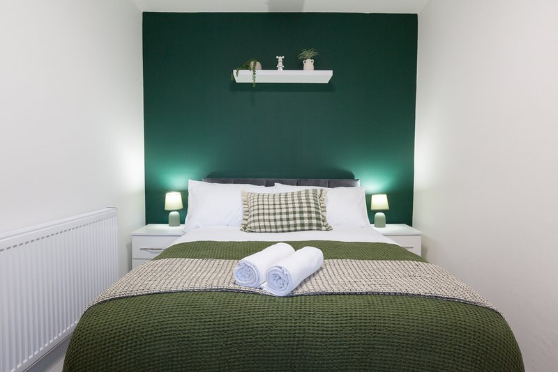 Modern bedroom with double bed, green feature wall, rolled towels, and bedside lamps