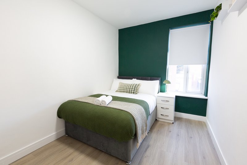 Bedroom with double bed, green accent wall, white bedside table and window