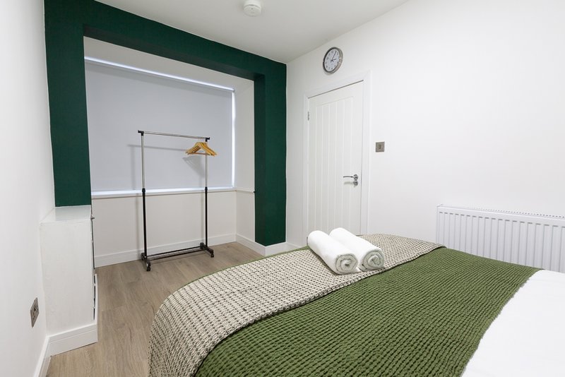 Modern bedroom with double bed, green and white bedding, wooden floor and dark green accent wall