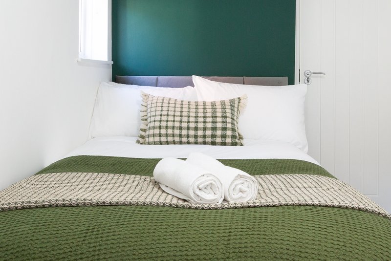 Bedroom with green headboard, white pillows, checkered cushion and rolled towels on bed