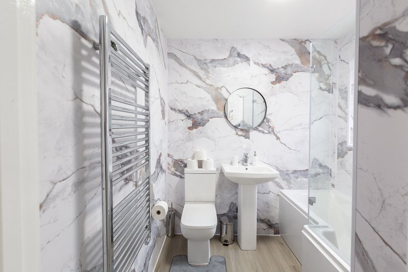 Modern bathroom with marble-effect tiles, pedestal sink, toilet, heated towel rail and round mirror
