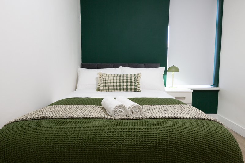 Bedroom with green headboard, white pillows, green bedspread and rolled white towels