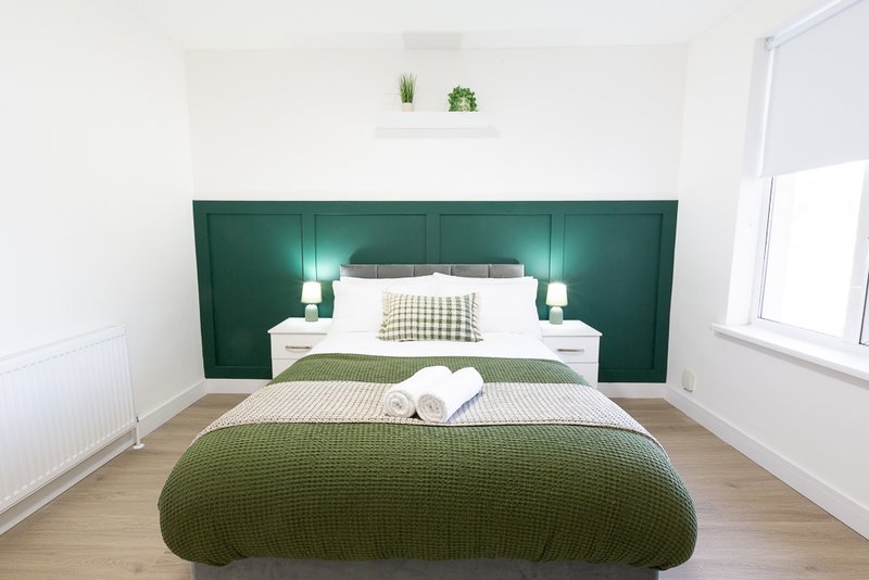 Modern bedroom with green upholstered headboard, double bed, wooden floor and side tables