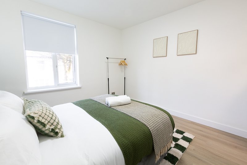 Bright bedroom with white bedding, green throw, patterned pillows and wooden floor