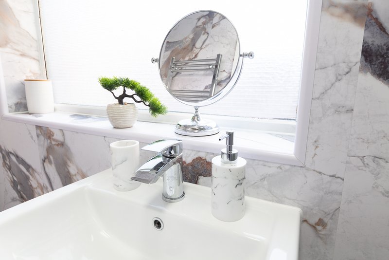 Modern bathroom sink with marble tiles, round mirror, and decorative plant