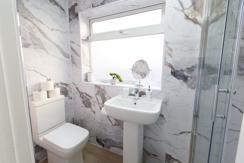 Modern bathroom with marble-effect walls, pedestal sink, toilet, and shower enclosure