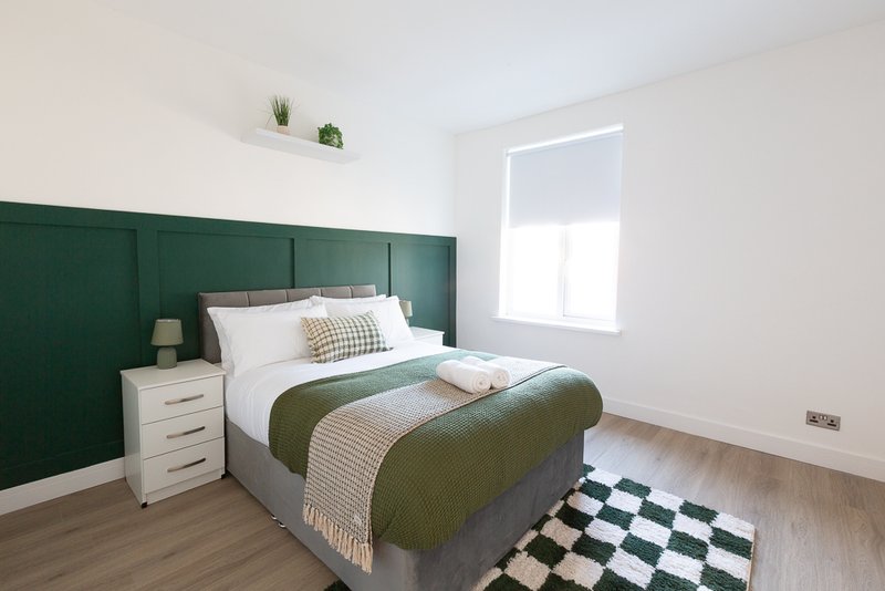 Modern bedroom with green headboard, double bed, white nightstand and checkered rug