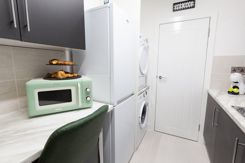 Modern kitchen with mint-green microwave, stacked washer-dryer, white cabinetry and countertops