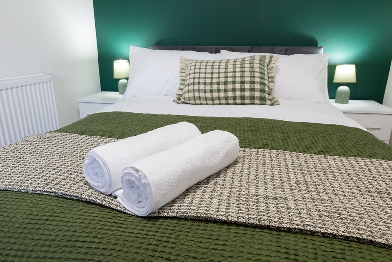 Bedroom with green accent wall, white bedding, rolled towels, and bedside lamps