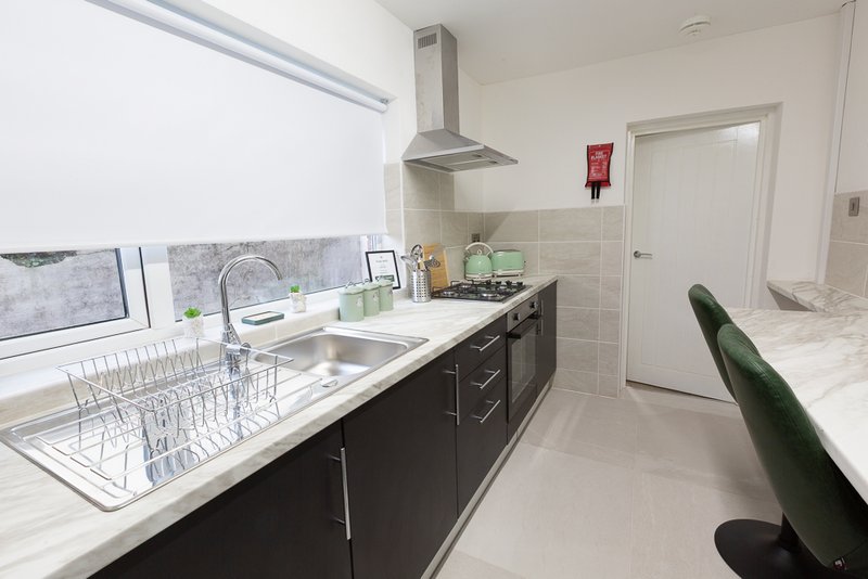Modern kitchen with dark cabinetry, stainless steel sink, extractor hood and white tiled backsplash