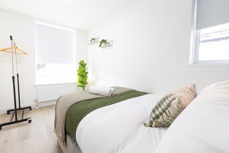 Bright bedroom with double bed, green bedding, patterned cushions and wooden floor