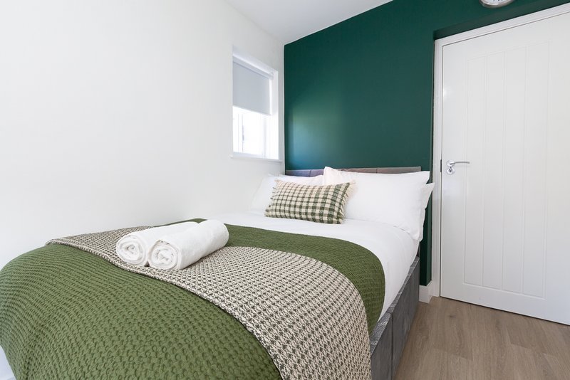 Bedroom with double bed, green headboard, rolled towels, and white door