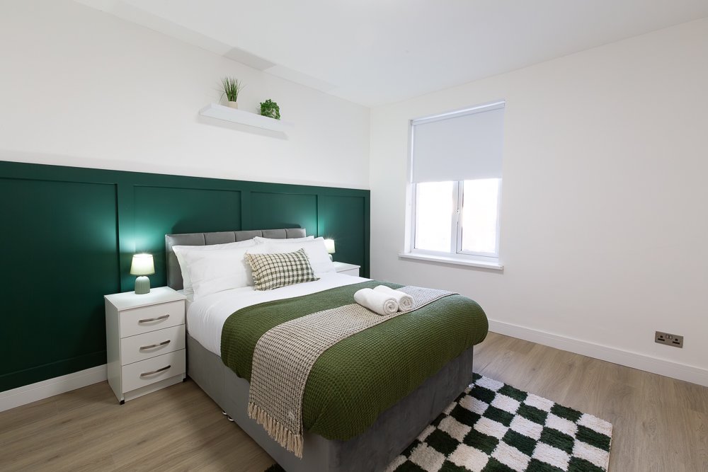 Modern bedroom with double bed, green headboard, white nightstand and black-and-white geometric rug