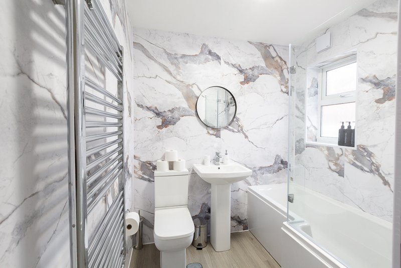 Modern bathroom with marble-effect tiles, pedestal sink, toilet, and round mirror