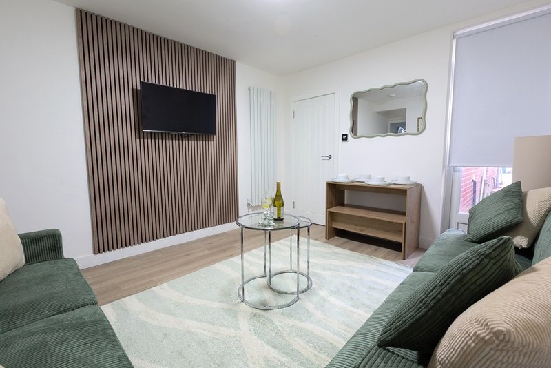 Modern living room with green upholstered sofa, wall-mounted TV, round glass table, and wooden dresser