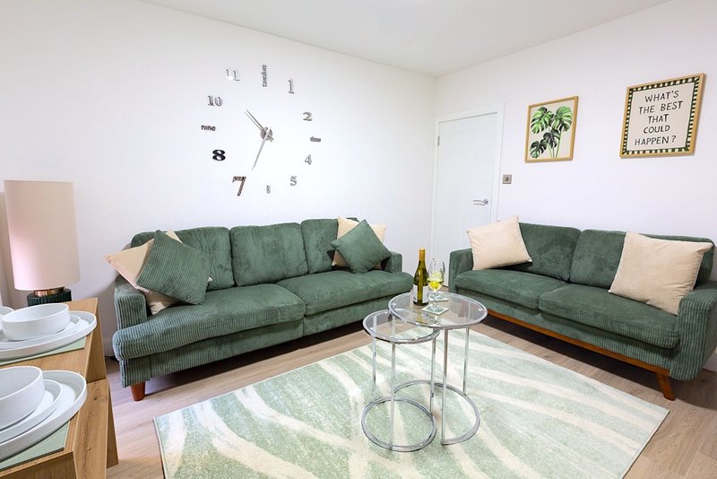 Modern living room with two green sofas, glass coffee table, wall clock and decorative artwork