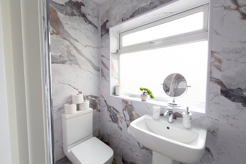 Modern bathroom with marble-effect tiles, white sink, toilet, mirror and window