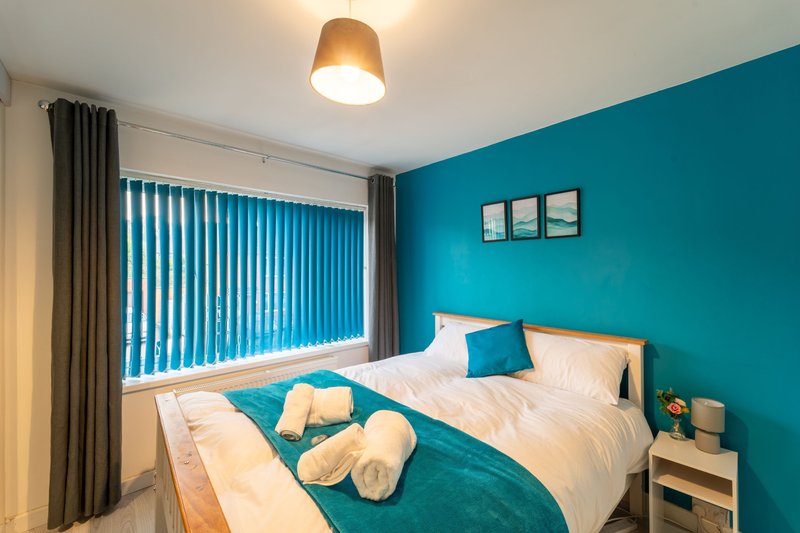 Modern bedroom with turquoise walls, double bed, wooden nightstand and vertical blinds