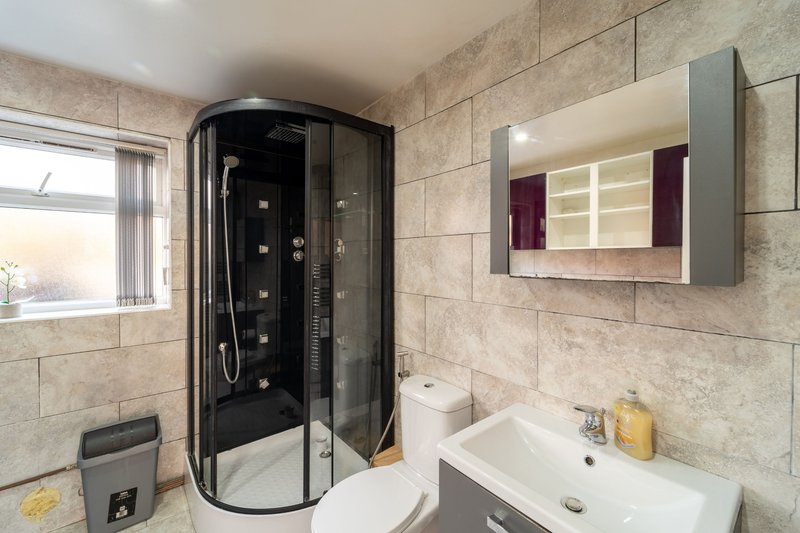 Modern bathroom with curved shower cubicle, white sink, mirror cabinet and tiled walls