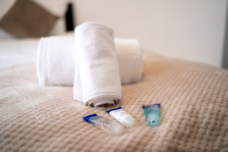 Bedroom detail with rolled white towels, toiletries and grooming items on bed