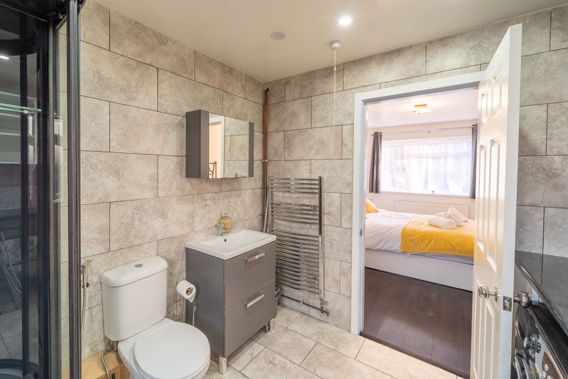 Modern bathroom with grey vanity, toilet, heated towel rail, and view to bedroom beyond