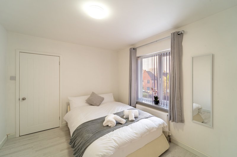 Bright bedroom with double bed, grey bedding, window with city view, and white doors