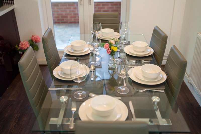 Modern dining room with glass table set for six, upholstered chairs, and French doors to garden