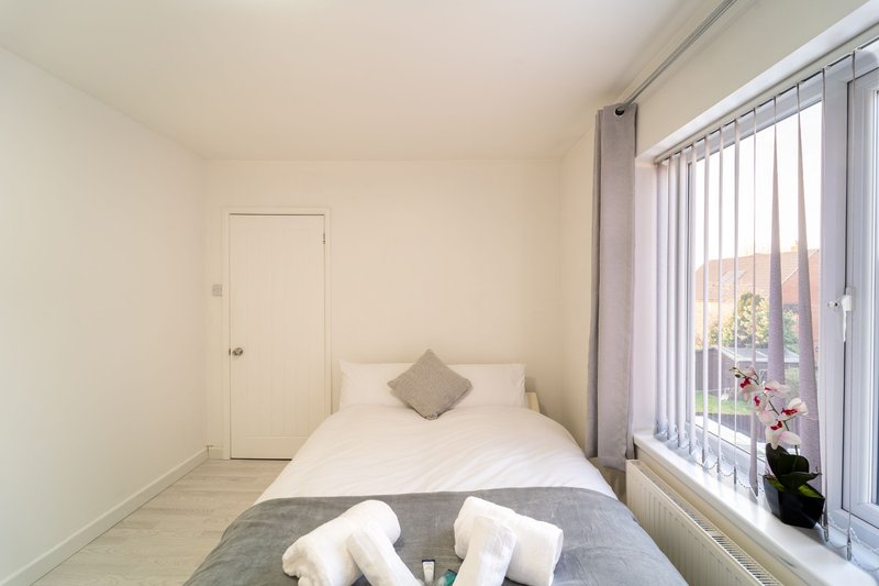 Bright bedroom with double bed, gray throw, white pillows, vertical blinds, and door
