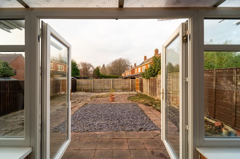 Garden view through open double doors with gravel patio and wooden fencing