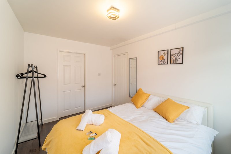 Bright bedroom with double bed, yellow bedding, white pillows, coat stand and framed wall art