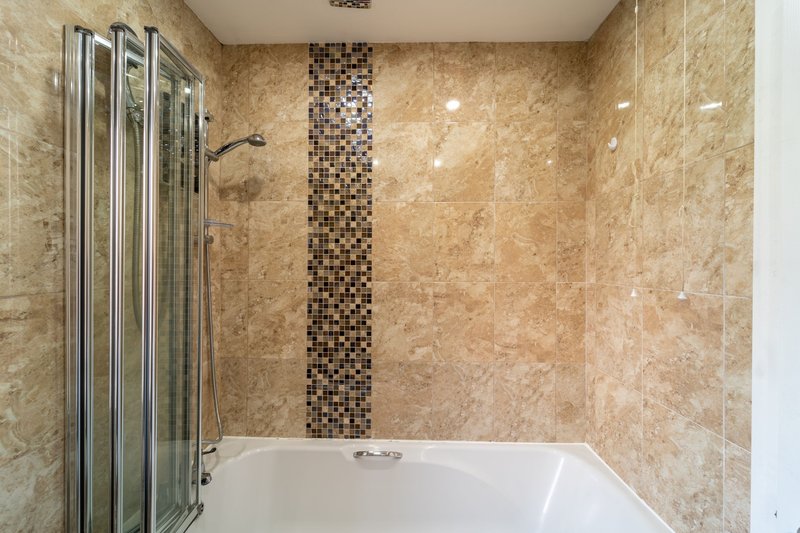 Bathroom with marble tile walls, white bathtub and glass shower enclosure