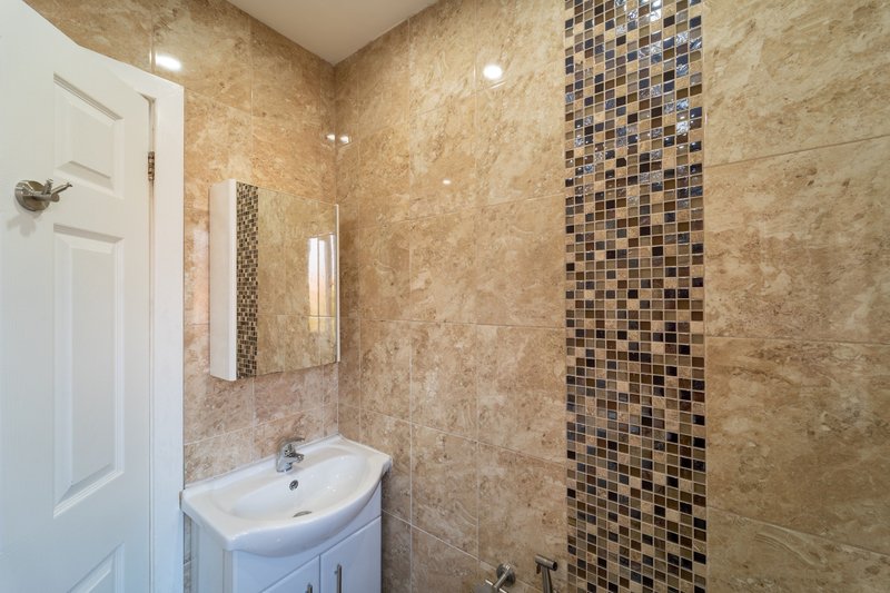 Modern bathroom with marble tile walls, pedestal sink, mirror and glass shower enclosure