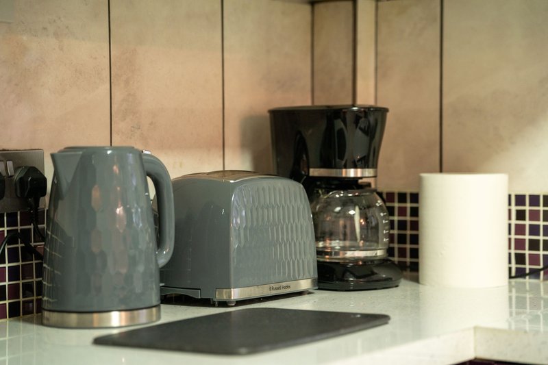 Kitchen countertop with grey kettle, toaster, coffee maker and white mug