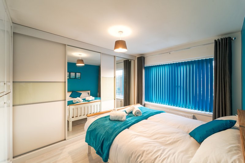 Modern bedroom with double bed, blue bedding, mirrored wardrobe and en-suite bathroom visible