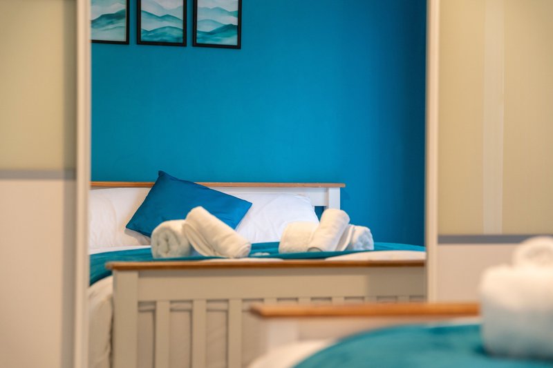 Modern bedroom with turquoise accent wall, white bedding, blue pillows and folded towels