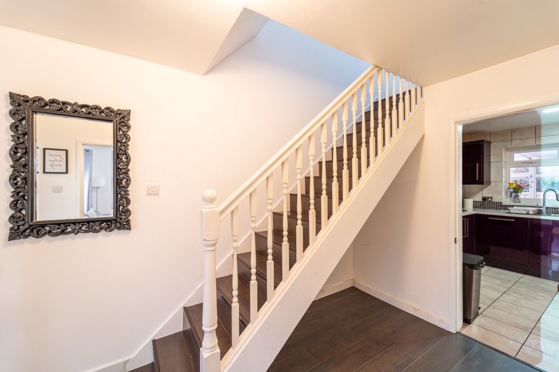 Hallway with wooden staircase, ornate mirror on wall, and kitchen doorway