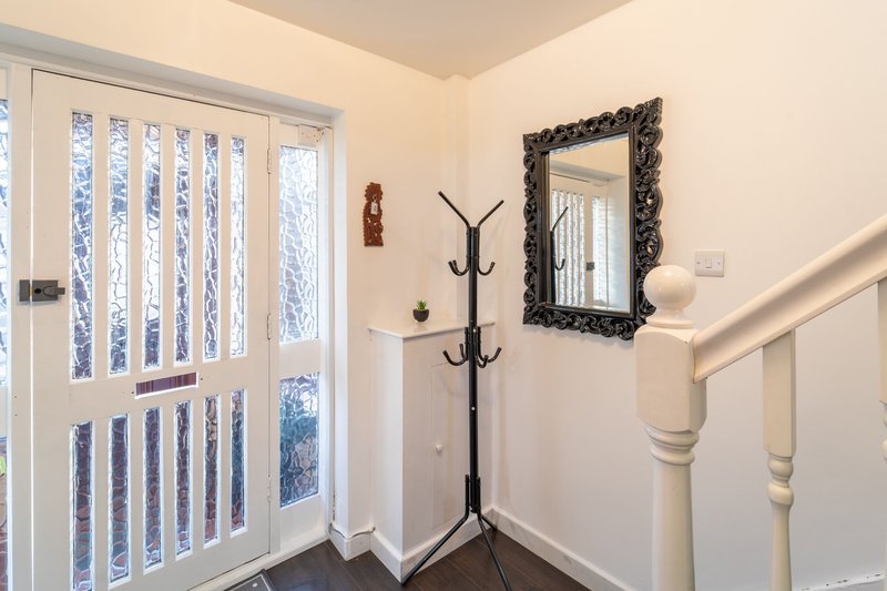 Bright hallway with white door, coat stand, ornate mirror and wooden staircase railing