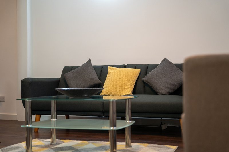 Modern living room with dark leather sofa, decorative cushions, glass coffee table