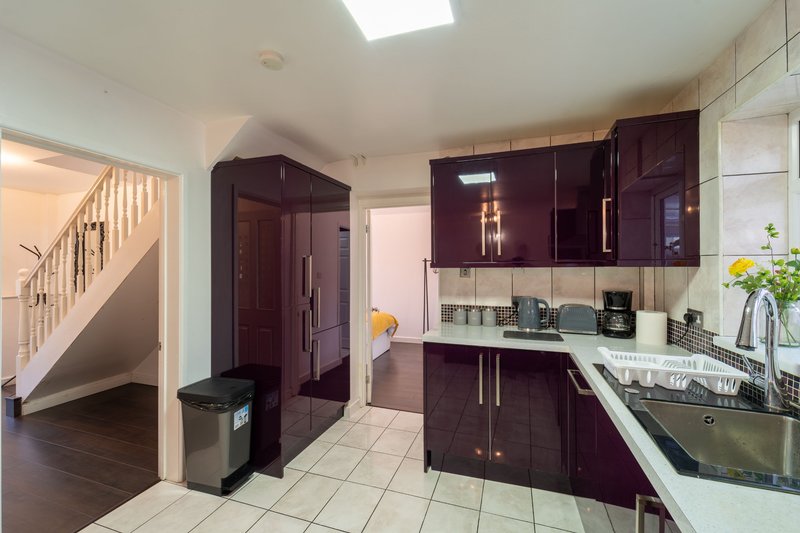 Modern kitchen with burgundy cabinets, white countertops, stainless steel appliances and staircase