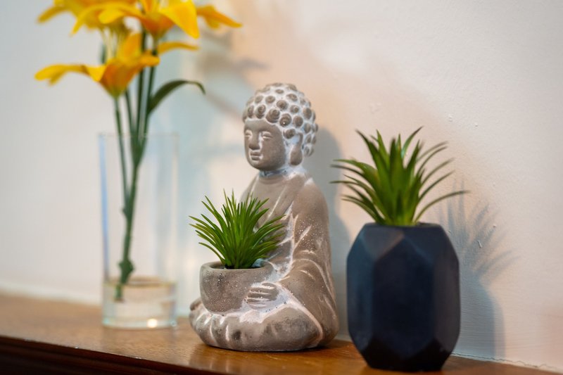 Decorative shelf with Buddha figurine, potted plants, and yellow flowers in vase